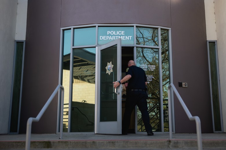 A police officer open the front door of a police deparment's building. The door includes the words "police department" along with the seal of the University of California police.