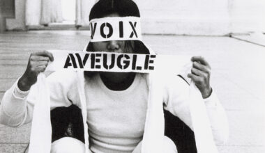 black and white image of woman squatting in white with eyes and mouth covered by 'voix' and 'aveugle'