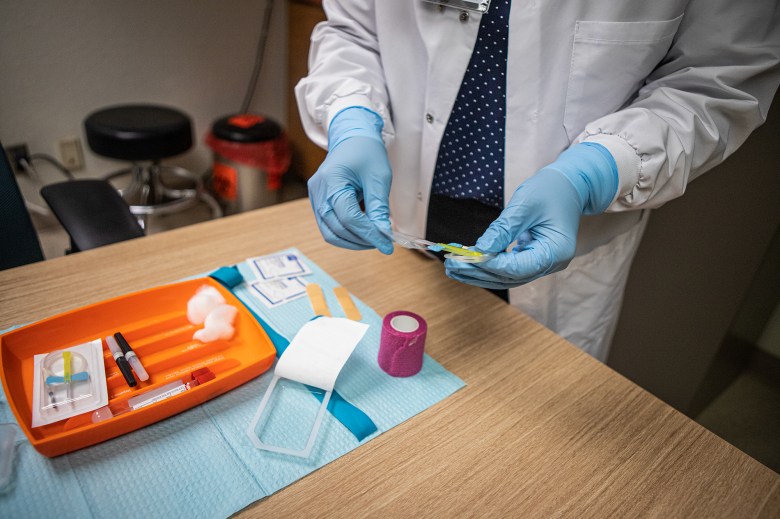 A nurse wearing blue medical gloves stands near a table as they prepare the equipment they need to conduct a blood draw.