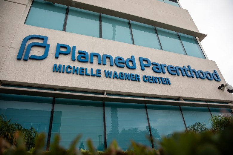 A Planned Parenthood letter sign outside a beige concrete building with glass windows.