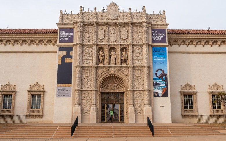 Three statues, portraits, shields, and other icons are displayed in the ornate facade of The San Diego Museum of Art.