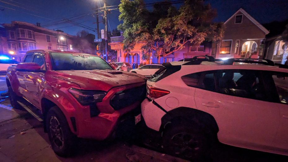A red truck and a white SUV are involved in a rear-end collision on a residential street at night, with police lights in the background.