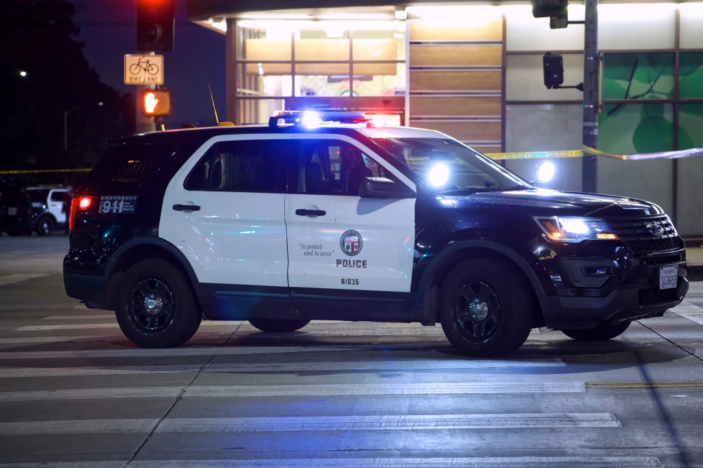A Los Angeles Police patrol car with glowing light bar at night on Sunset Boulevard.