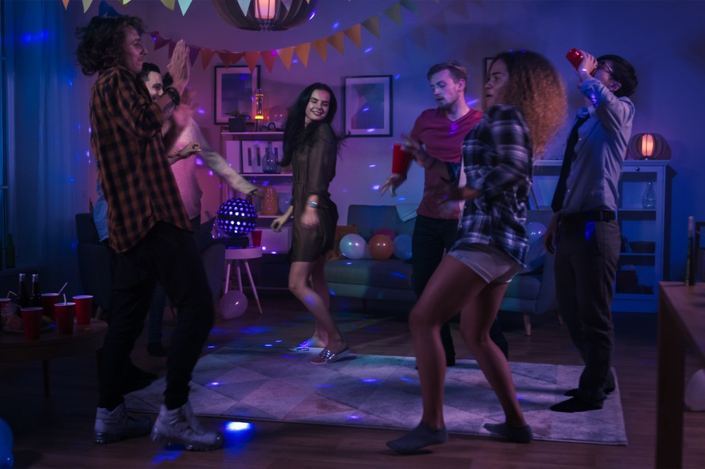 Friends dance at a party in a dimly lit room with purple lighting.