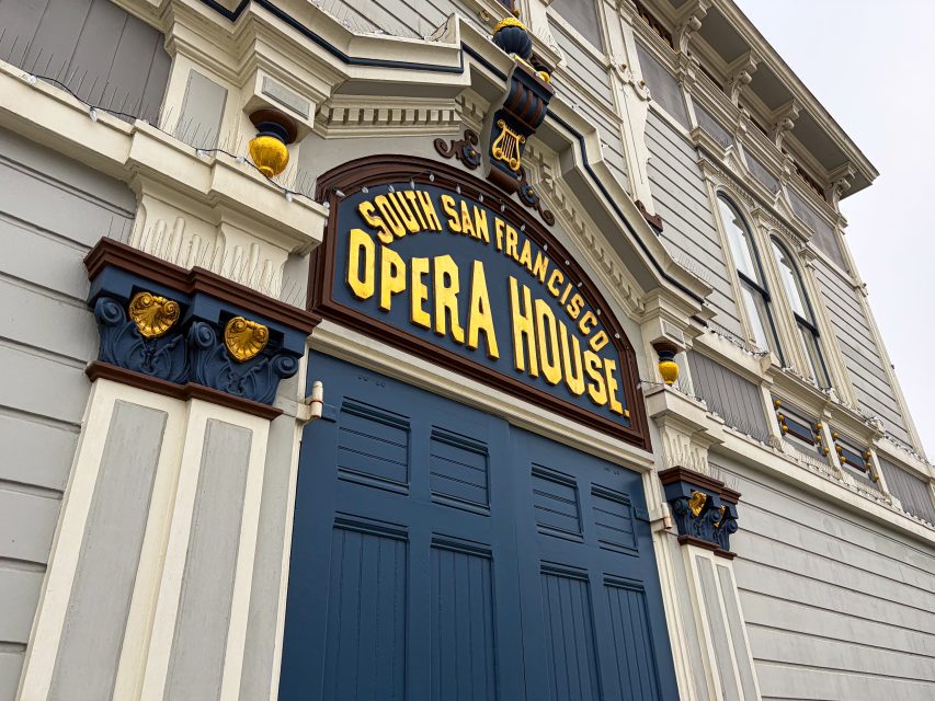 Close-up of the entrance to the South San Francisco Opera House, featuring detailed architectural features and a prominent yellow and blue Bayview Buzz sign above striking blue double doors.
