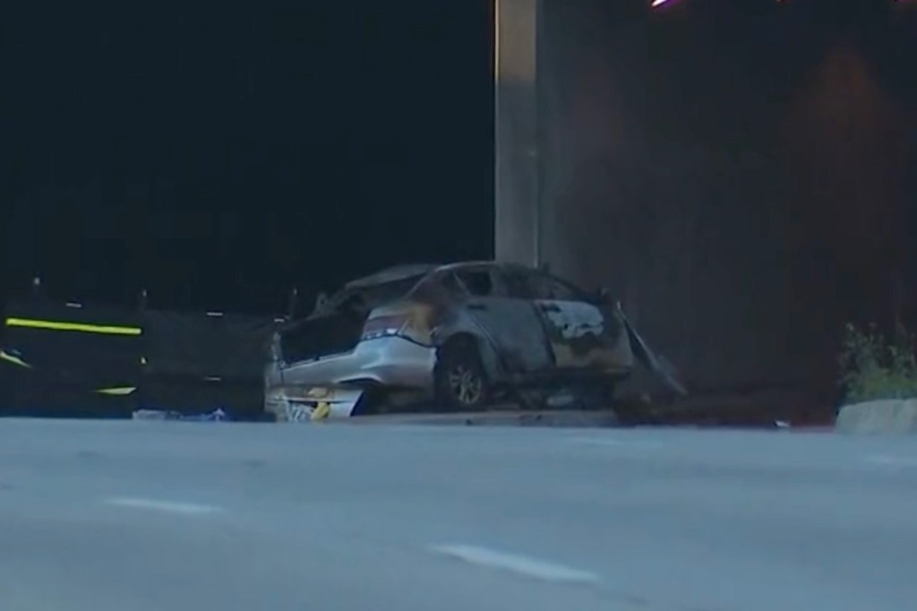 A burned-out car on the side of a road at night.