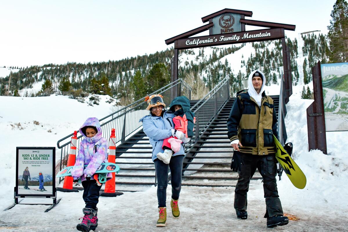 A family of four in snowboarding gear with a snow-covered mountain in the background.
