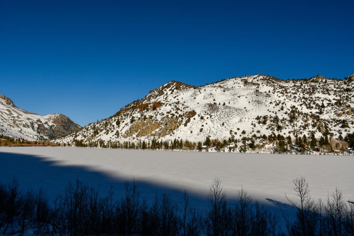 A frozen lake with tree spotted, snow covered mountains surrounding it.