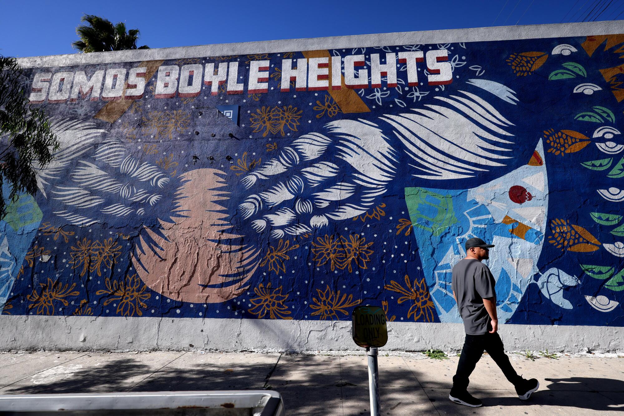 A man walks past a mural that reads, "Somos Boyle Heights." 