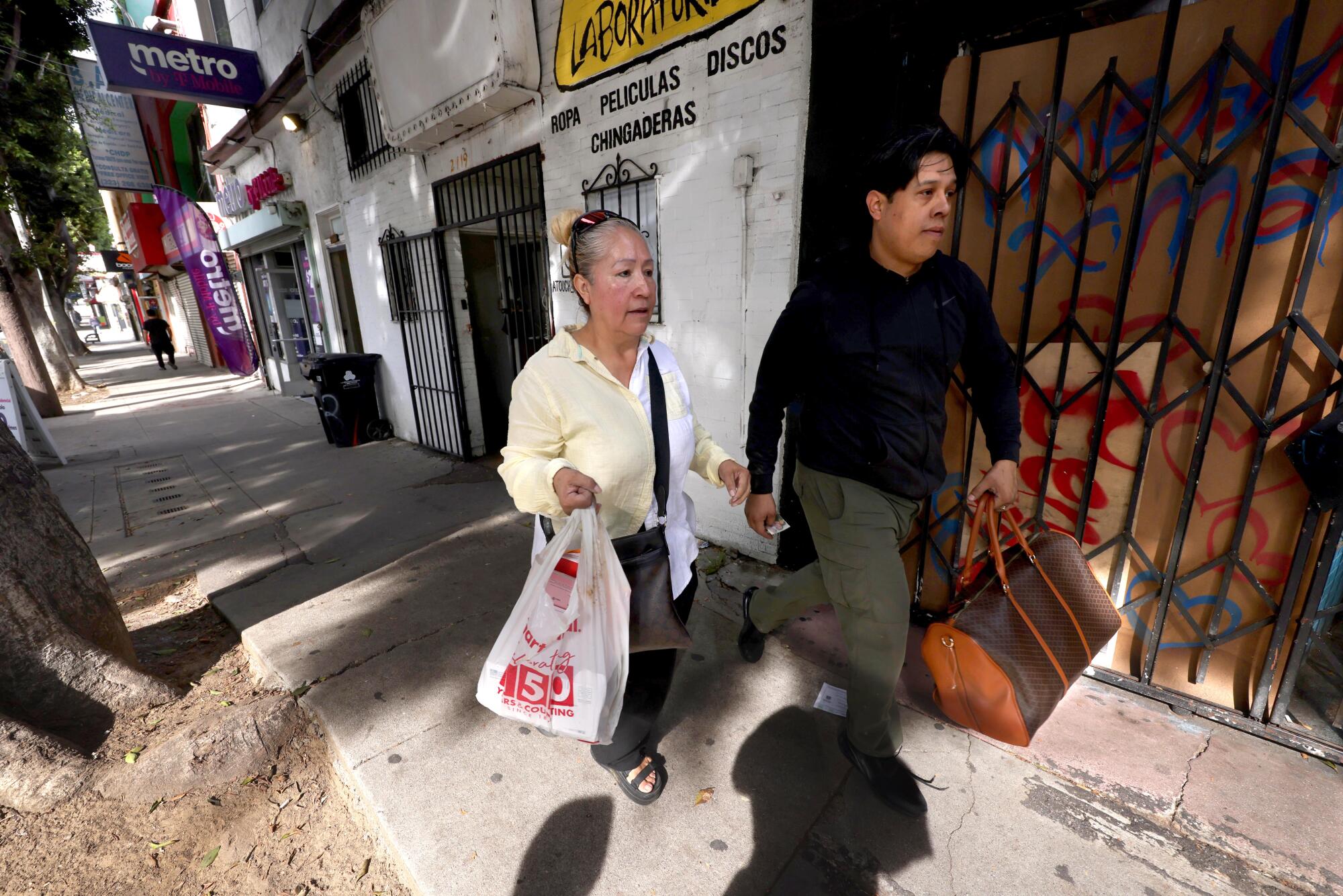 A man and woman carry bags as they walk along a sidewalk.
