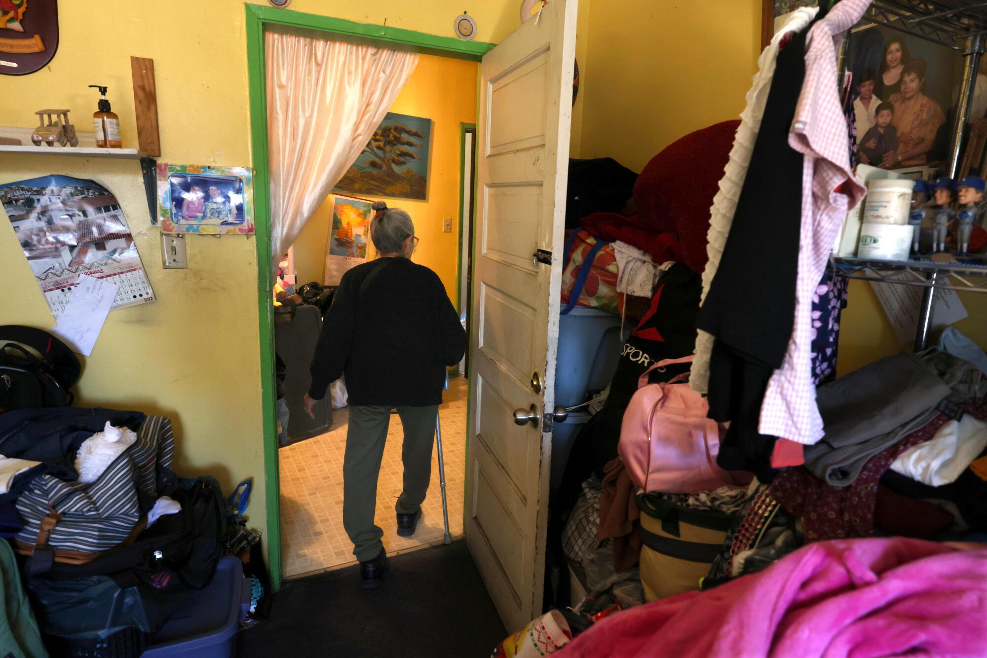 A woman with a cane walks through a doorway.
