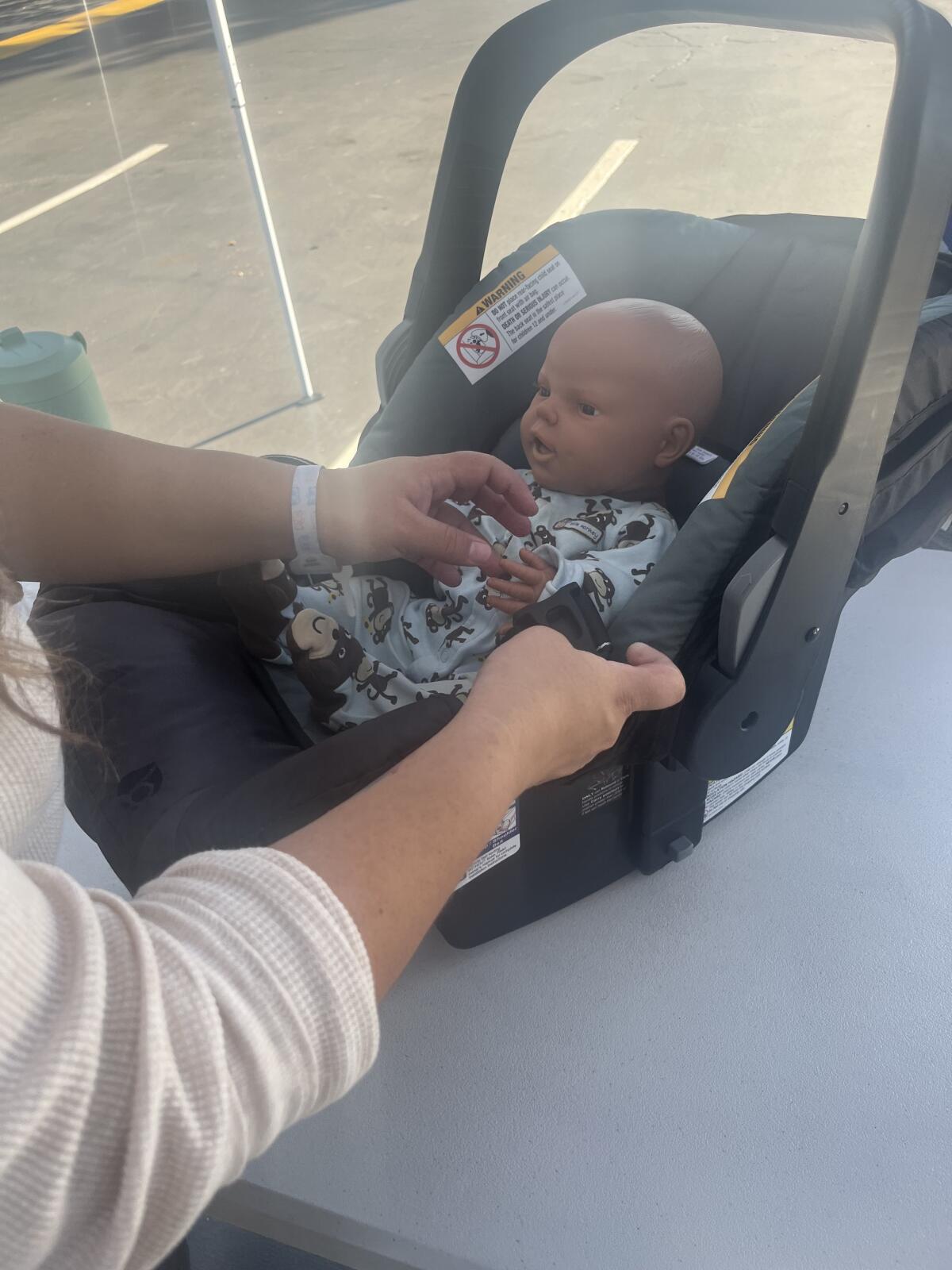 A mom practices placing an infant in a car seat at the UCI Health car seat event.
