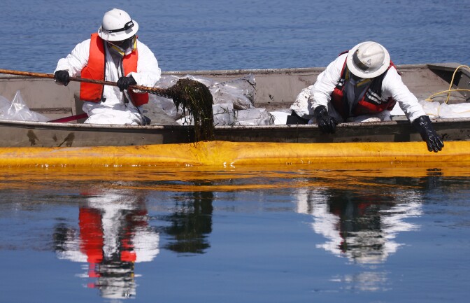 People in protective suits in a boat pull gloopy oil out of the ocean.