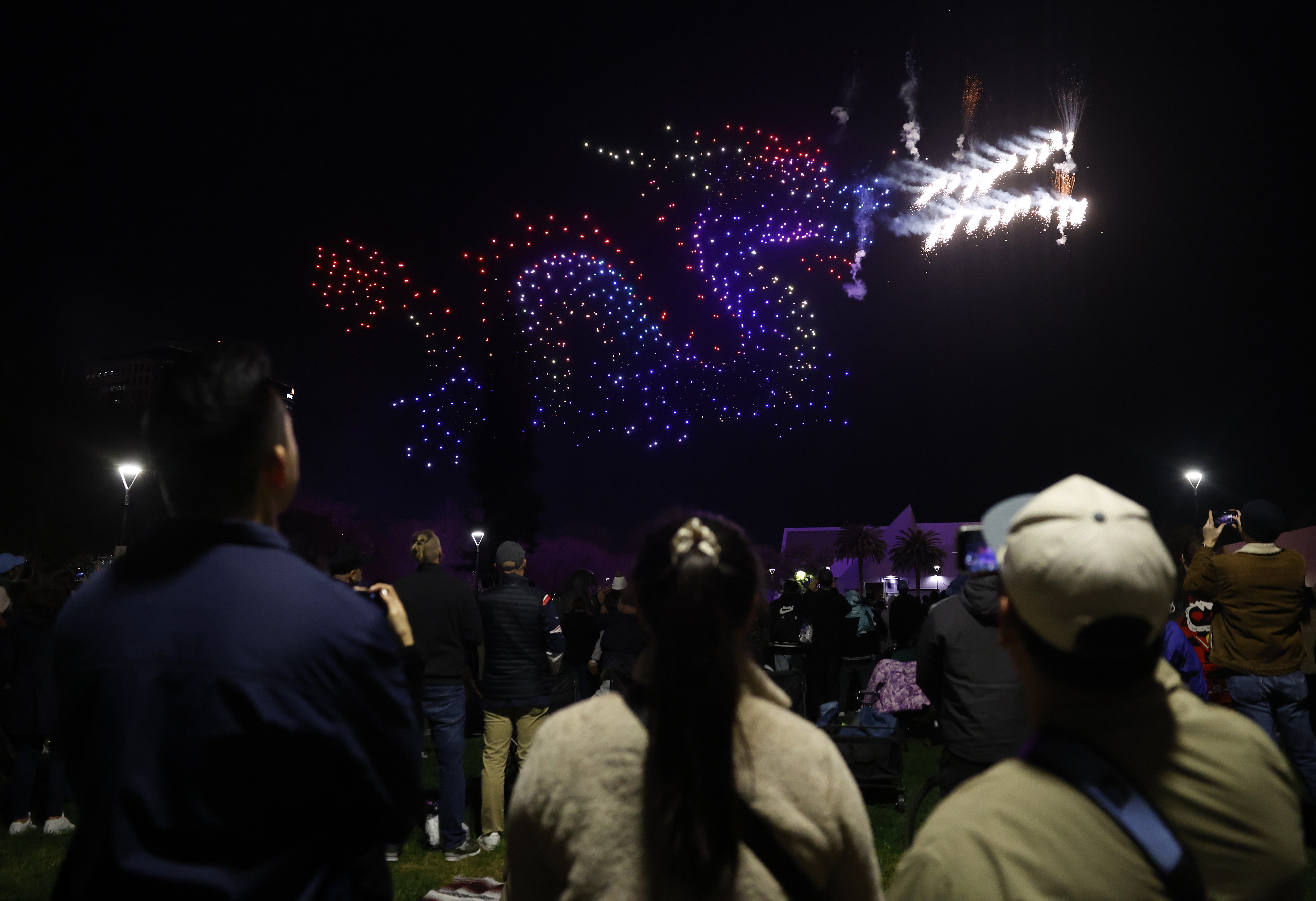People watch a drone show which depicts a dragon in...
