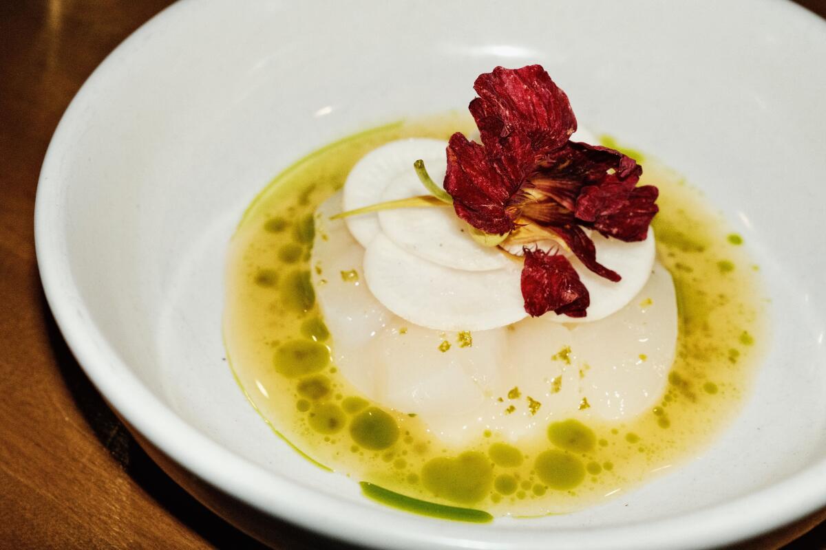 Slices of raw Hokkaido scallop in a yellow-and-green broth, all topped with a flower