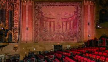 An ornate, circular ceiling with floral and geometric patterns surrounds a central, white, star-shaped chandelier, above intricately carved walls.