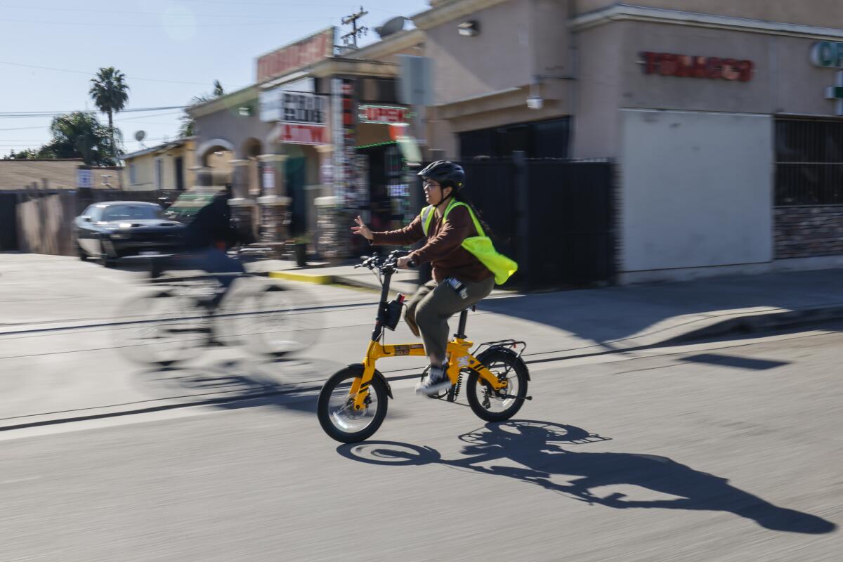 A woman waves while biking on a city street.