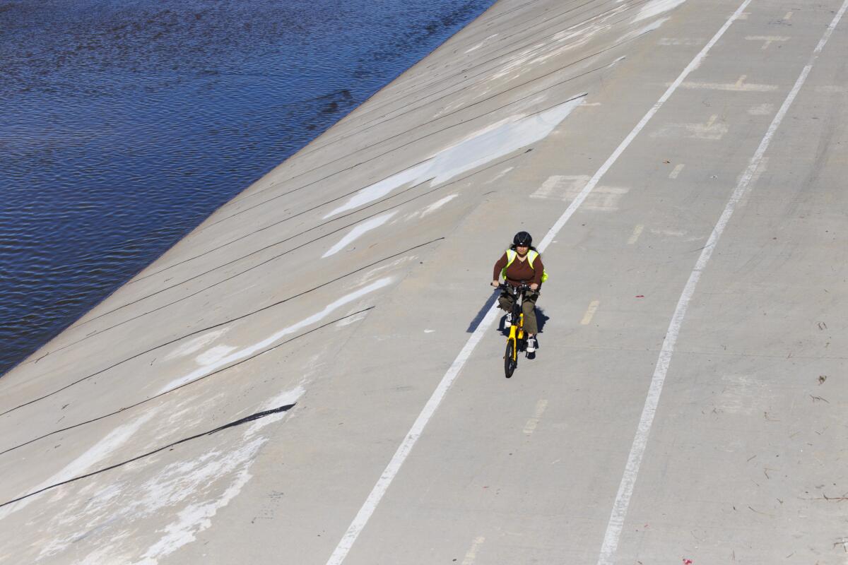 A woman bikes along a bike path next to a river on a sunny day.