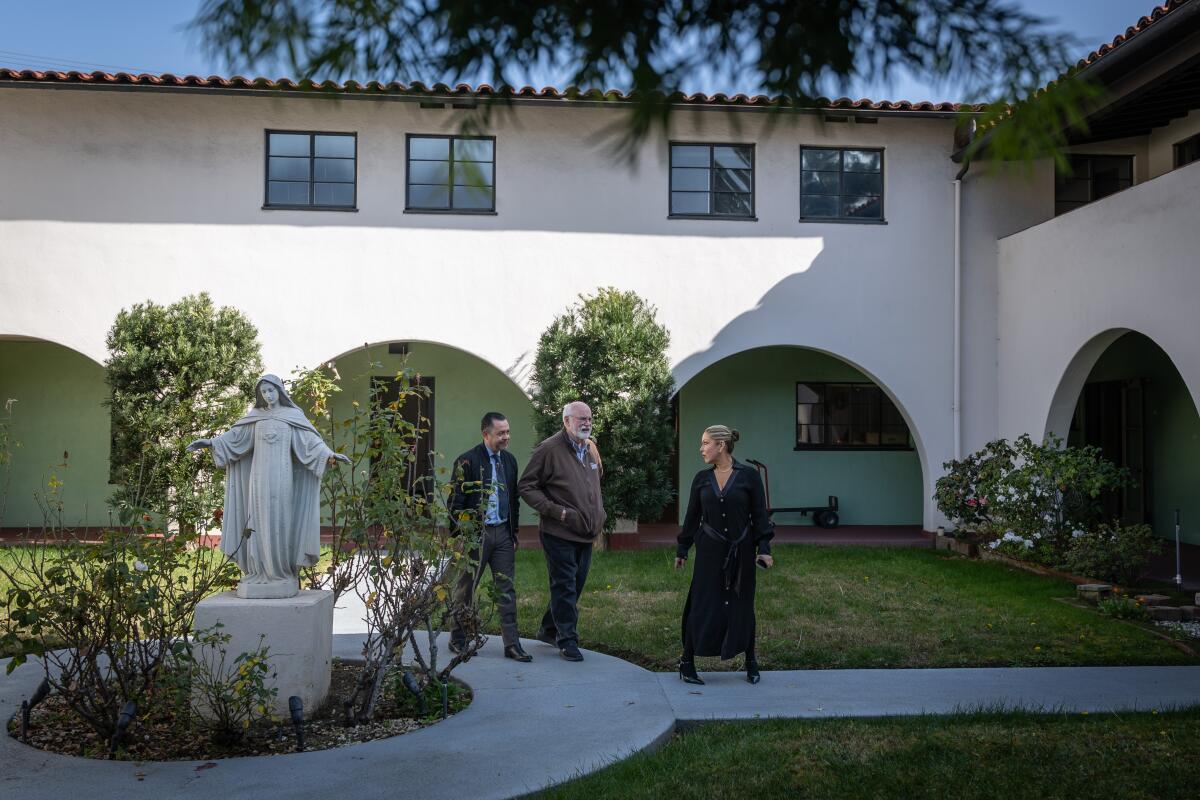 Father Greg Boyle and two other people walk through the courtyard of the Monastery of the Angels.