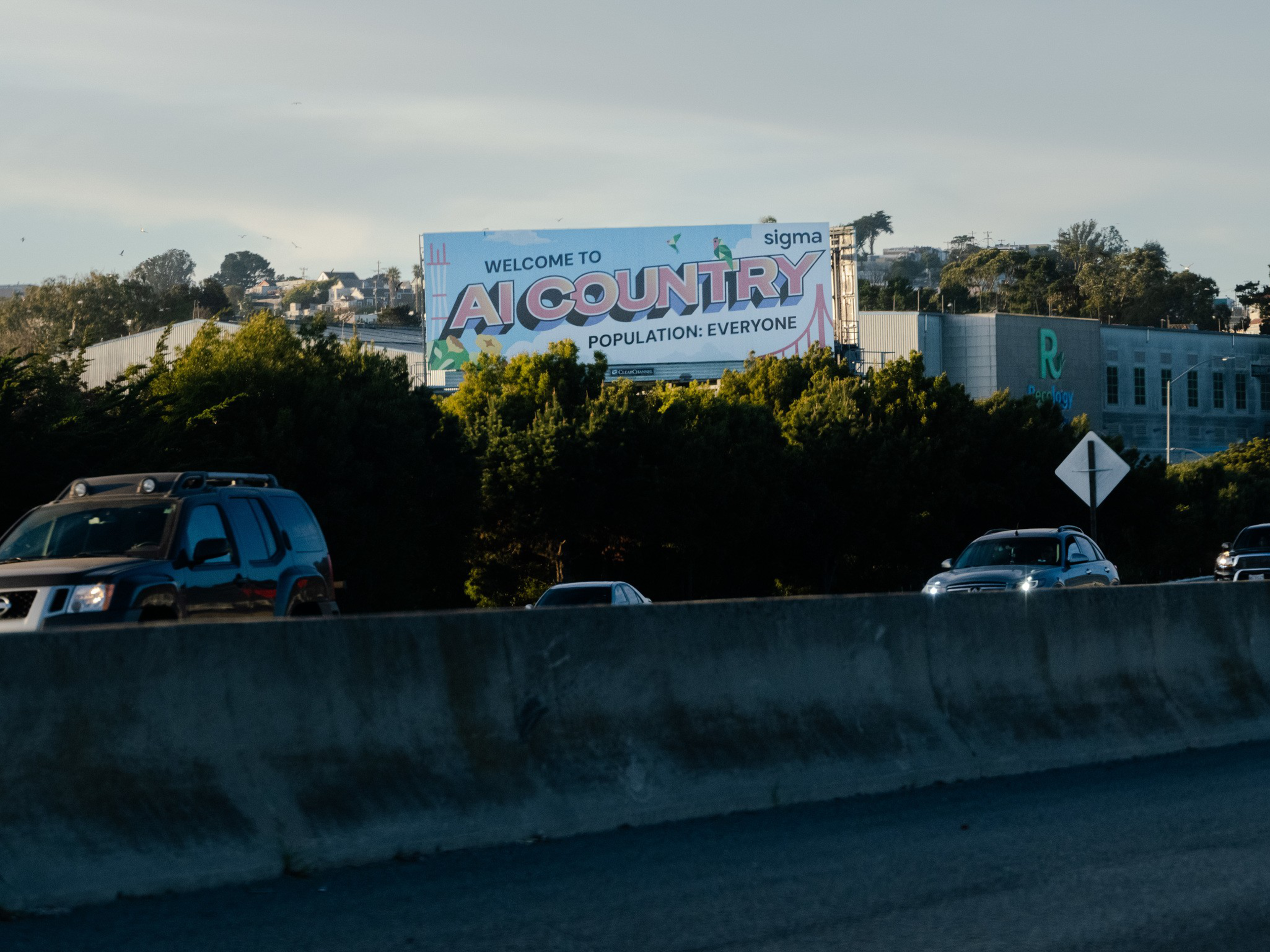 A billboard above a highway reads, “Welcome to AI Country, Population: Everyone,” surrounded by trees and several cars on the road.