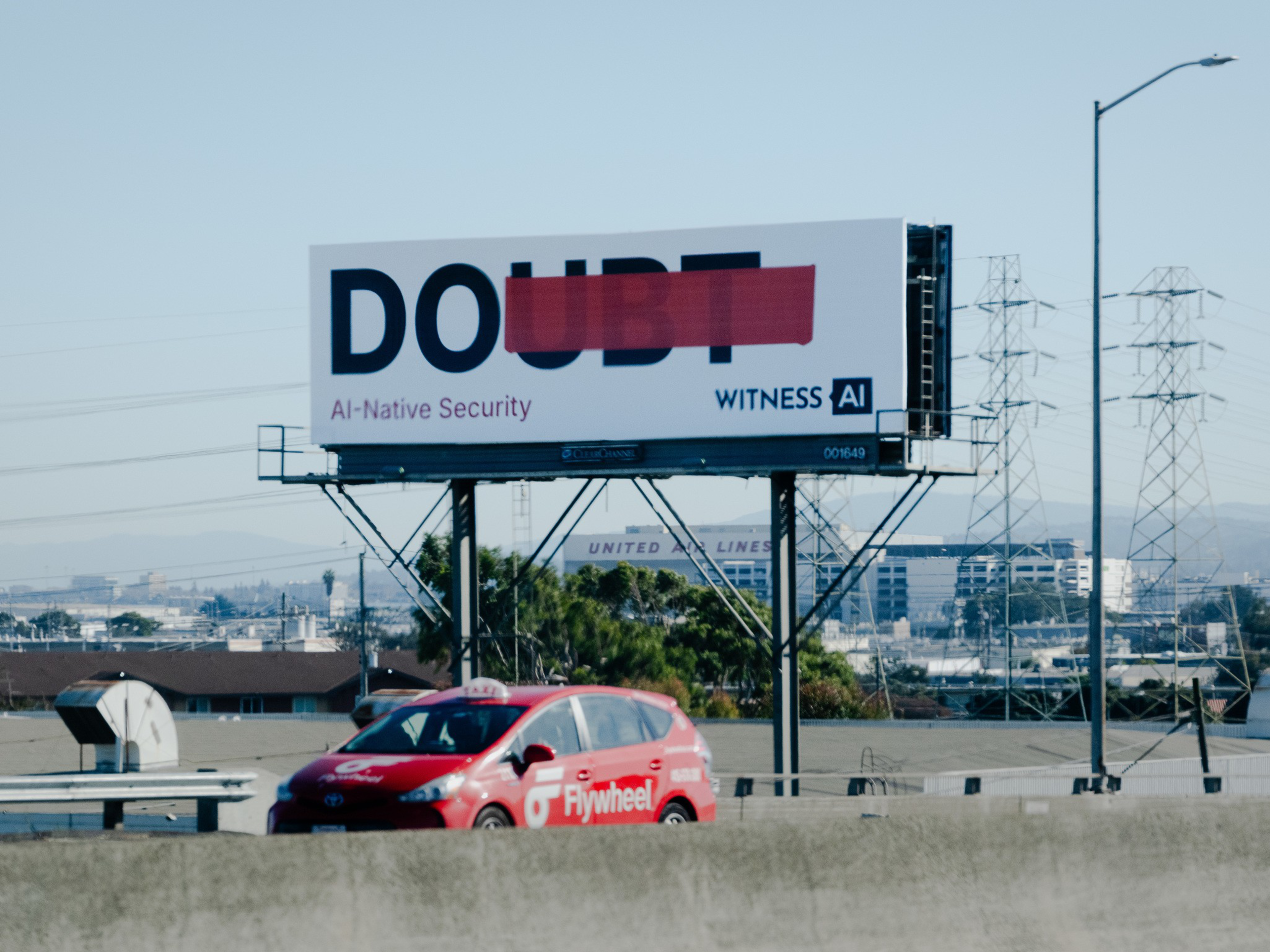 The word “DOUBT” appears on a billboard with “UBT” crossed out in red, alongside “AI-Native Security” and “Witness AI” text, above a red Flywheel car.