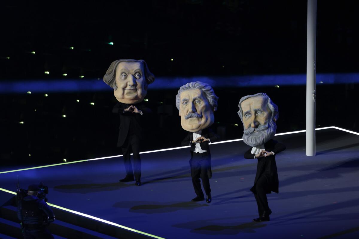 Three dancers in black wearing giant heads of older men.