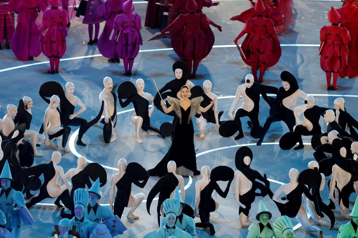 Dancers in white and black leotards surround a conductor in the middle of a stage.