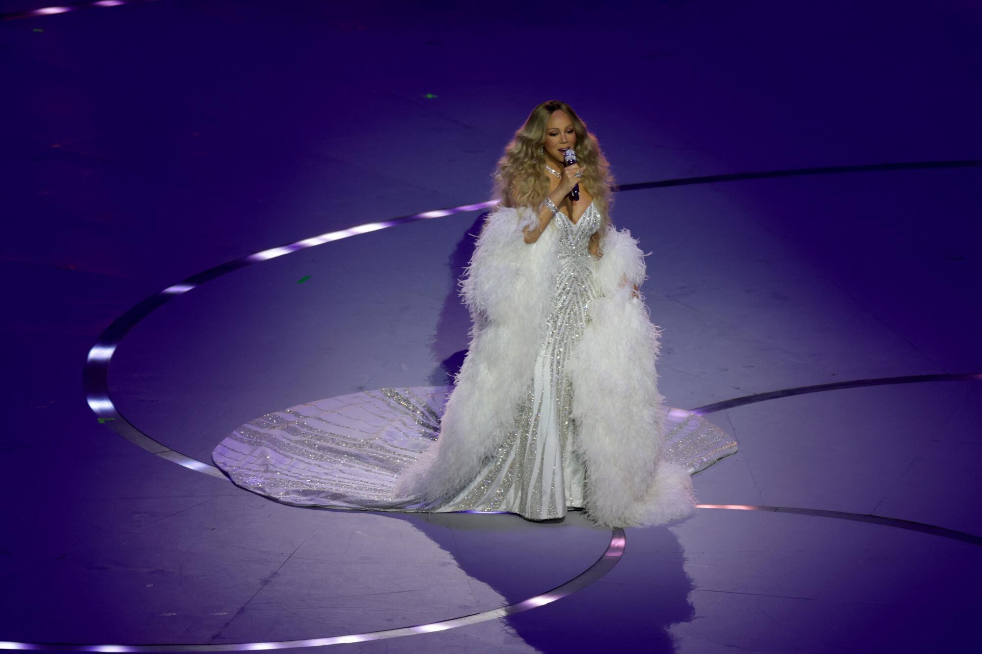 A woman in a white gown singing on a stage.