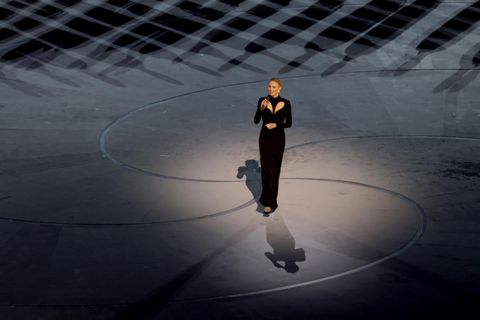 A woman in a black gown stands on a stage with a microphone.