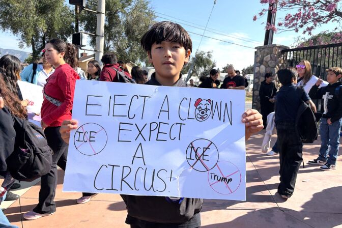 A boy with medium skin tone holds up a sign that says "elect a clown, expect a circus."