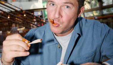 A meal spread includes a bowl of stew with a large tortilla chip, two tacos with various toppings, a wrapped sandwich, a creamy dipping sauce, a green bottle, and a lime drink.