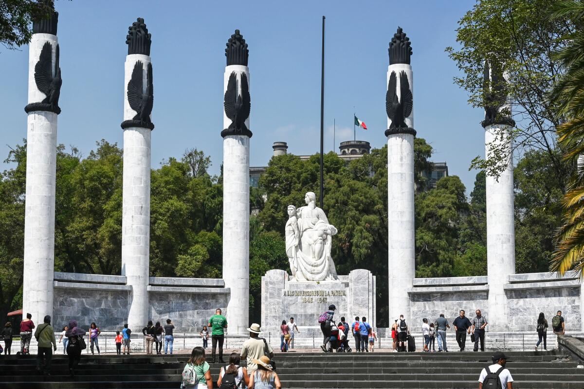 People at a monument featuring pillars with black adornments flanking a statue on a base