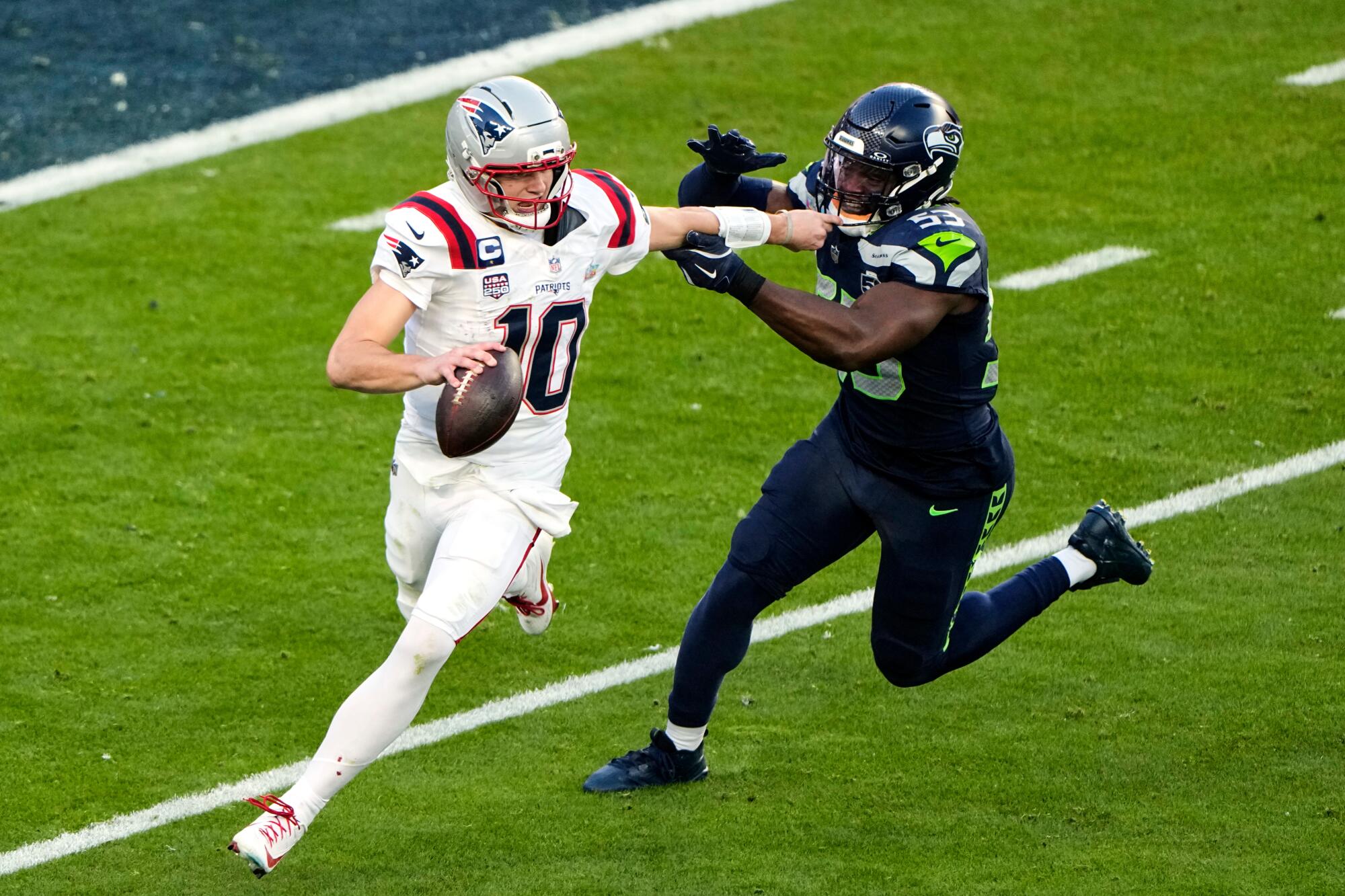 New England Patriots quarterback Drake Maye, left, fights off pressure from Seattle Seahawks linebacker Boye Mafe.