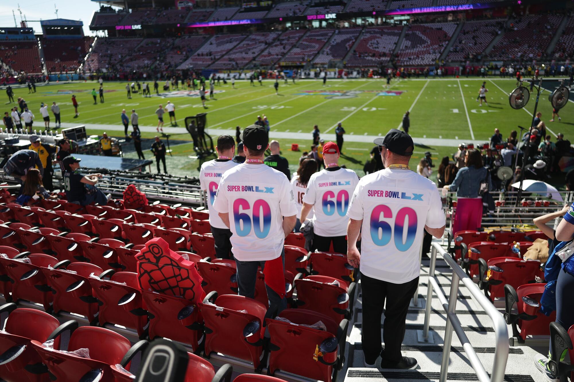 People walk into a sunny football stadium wearing "60" shirts.