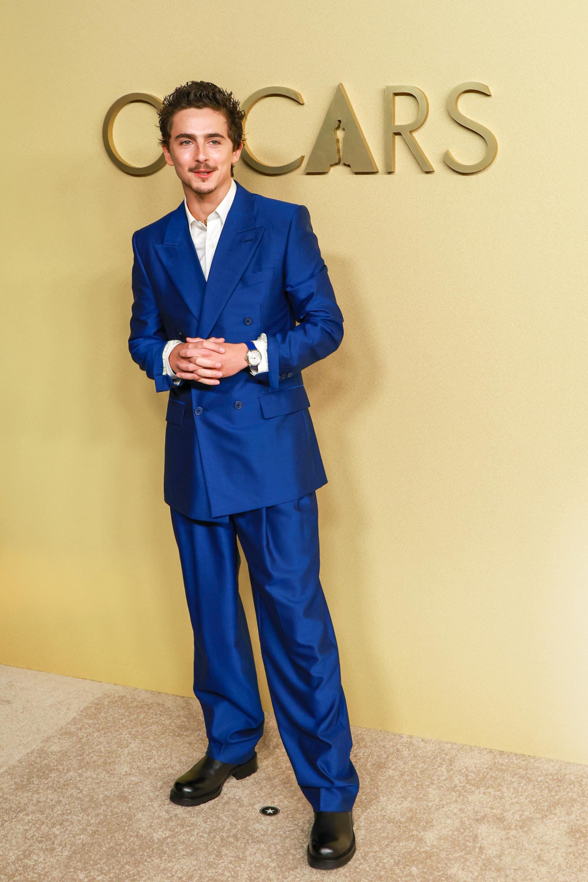 Timothée Chalamet, wearing an electric blue suit, poses on the beige carpet. 