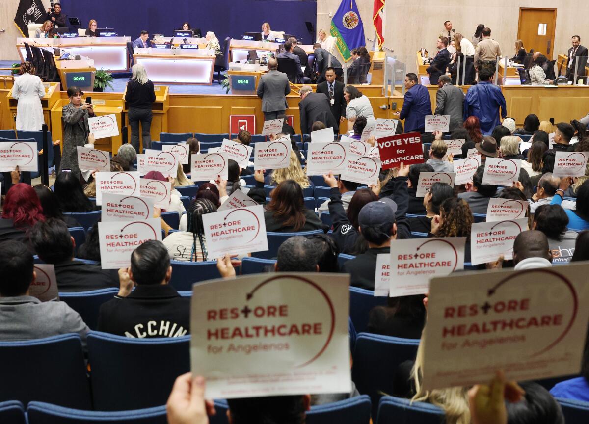 Audience members hold up signs inside the L.A. County Hall of Administration