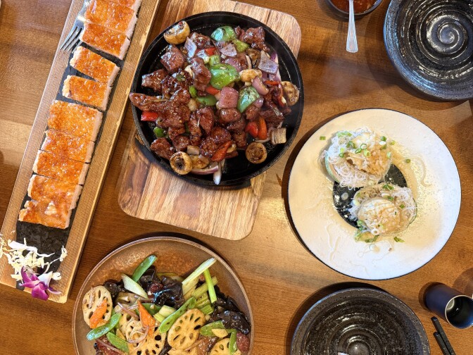 An array of colorful Chinese dishes are laid out on a wooden table