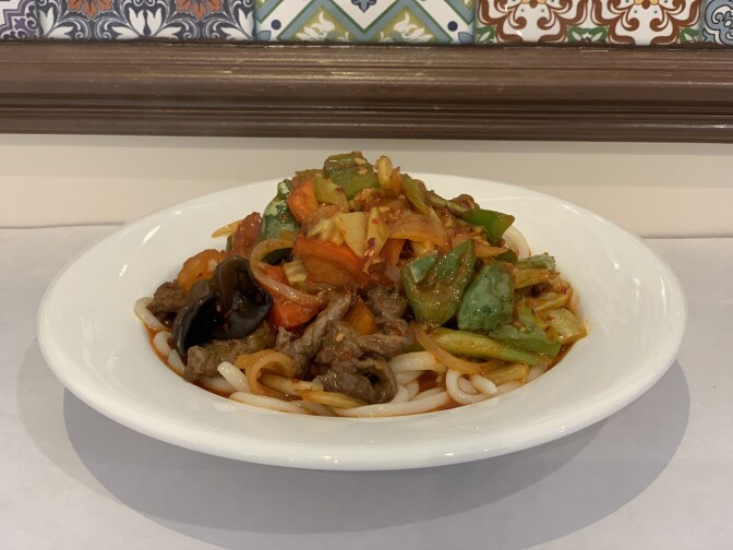 A white plate contains a pile of noodles, brown meat and stir-fried vegetables