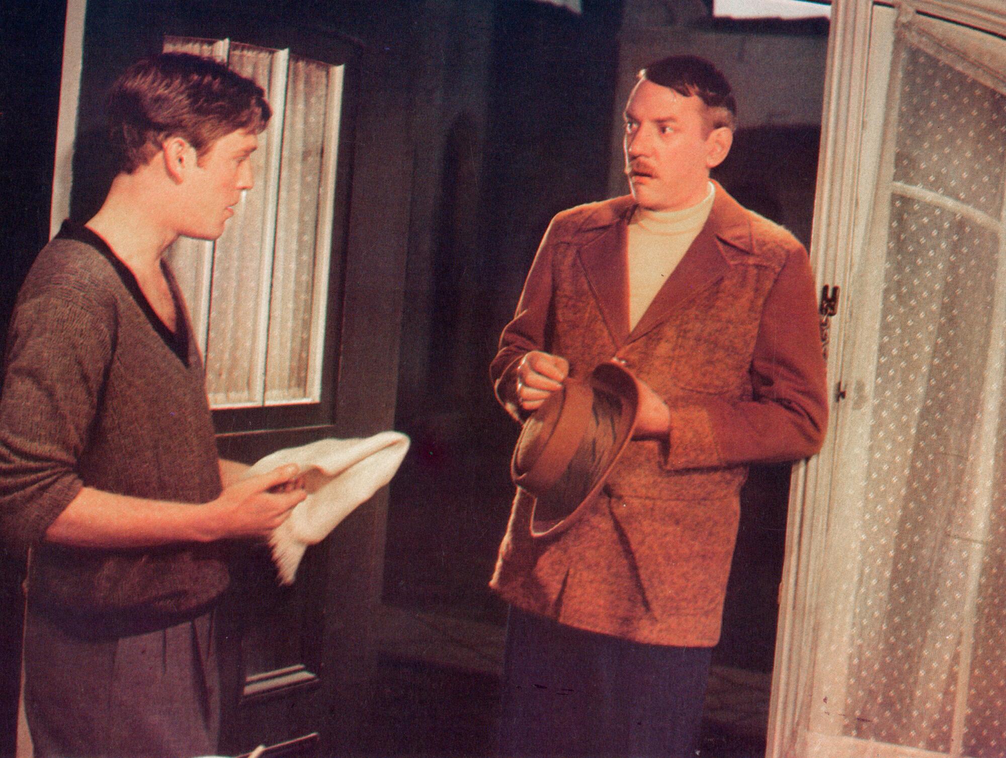 Two men speak to each other in a foyer.