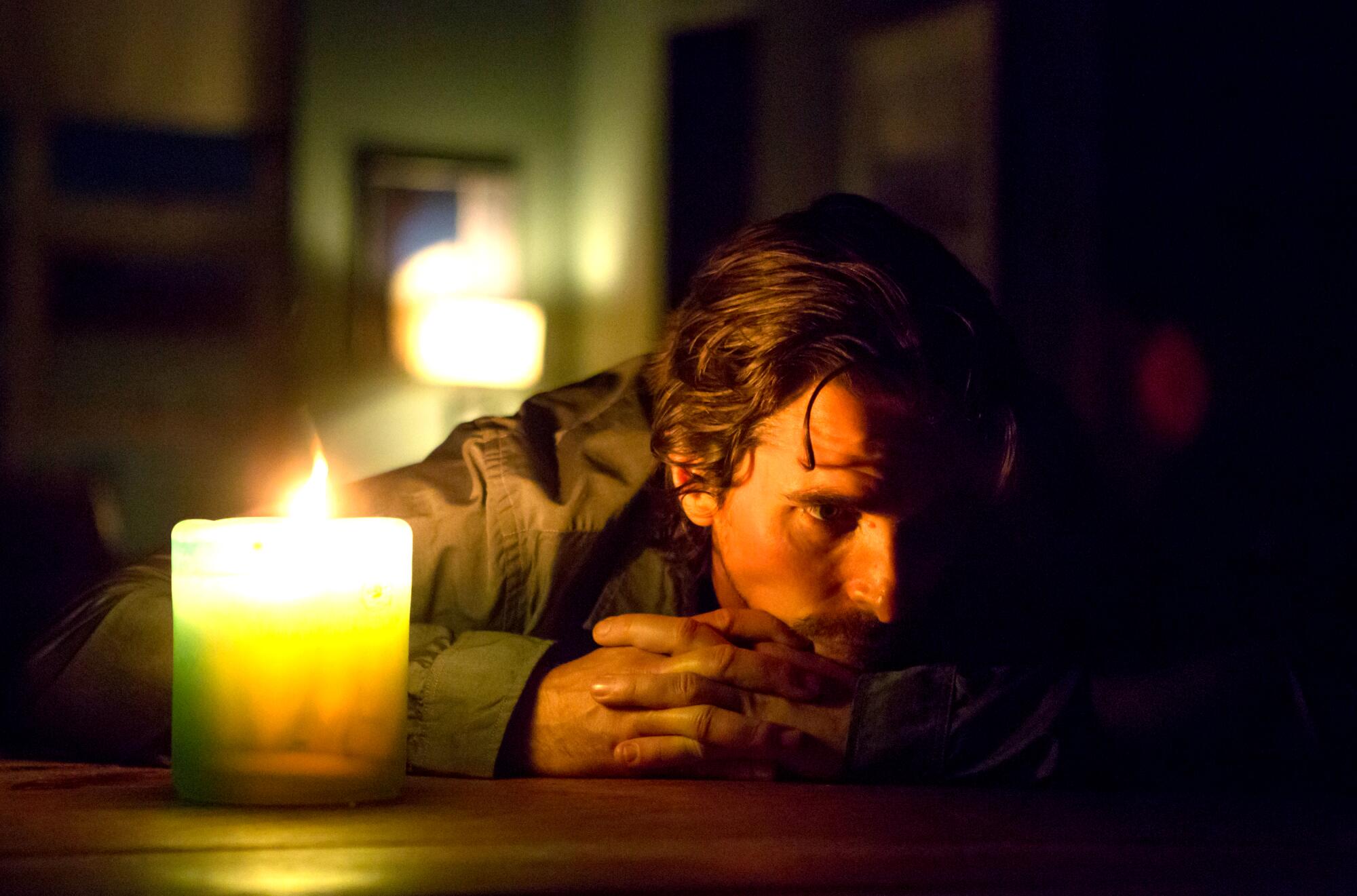 A man rests his chin on table behind a candle.