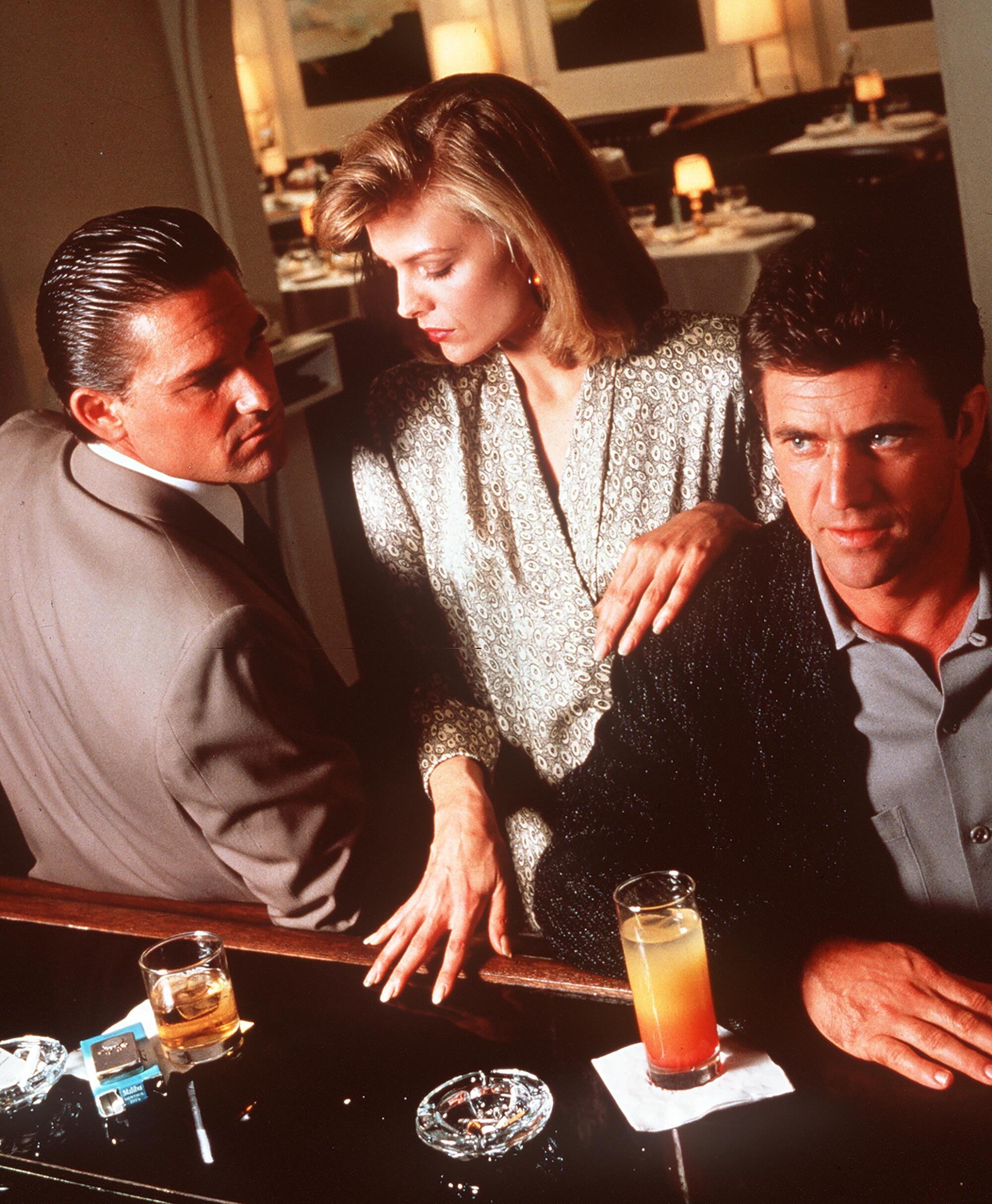 Three people stand at a bar.