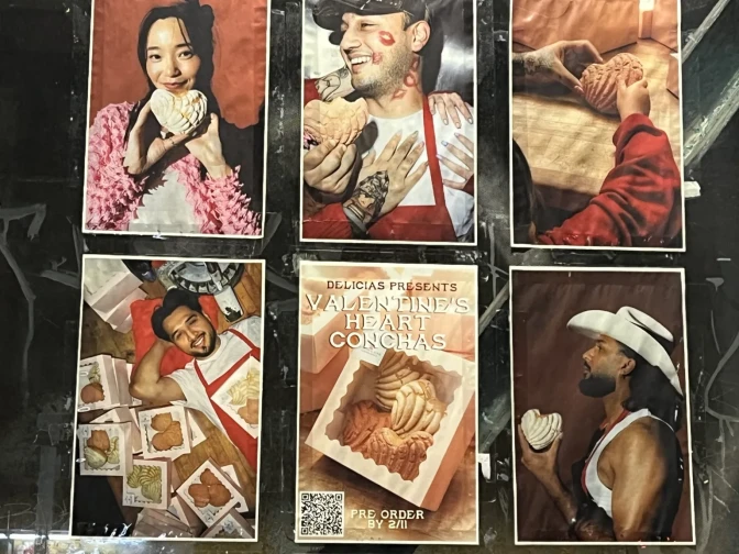Six posters are displayed on a window. The posters show people holding heart-shaped concha pan dulce and a box displaying the Mexican sweet bread with text that read "Delicias presents Valentine's Heart Conchas."