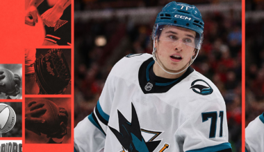 A hockey player wearing a white San Jose Sharks jersey with number 71 and a blue helmet skates on the ice with a focused expression.