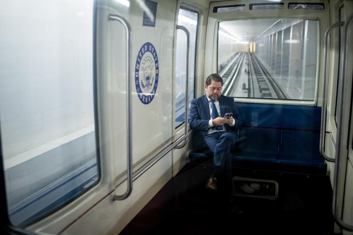 a man in a suit looks at a phone while riding the Senate subway