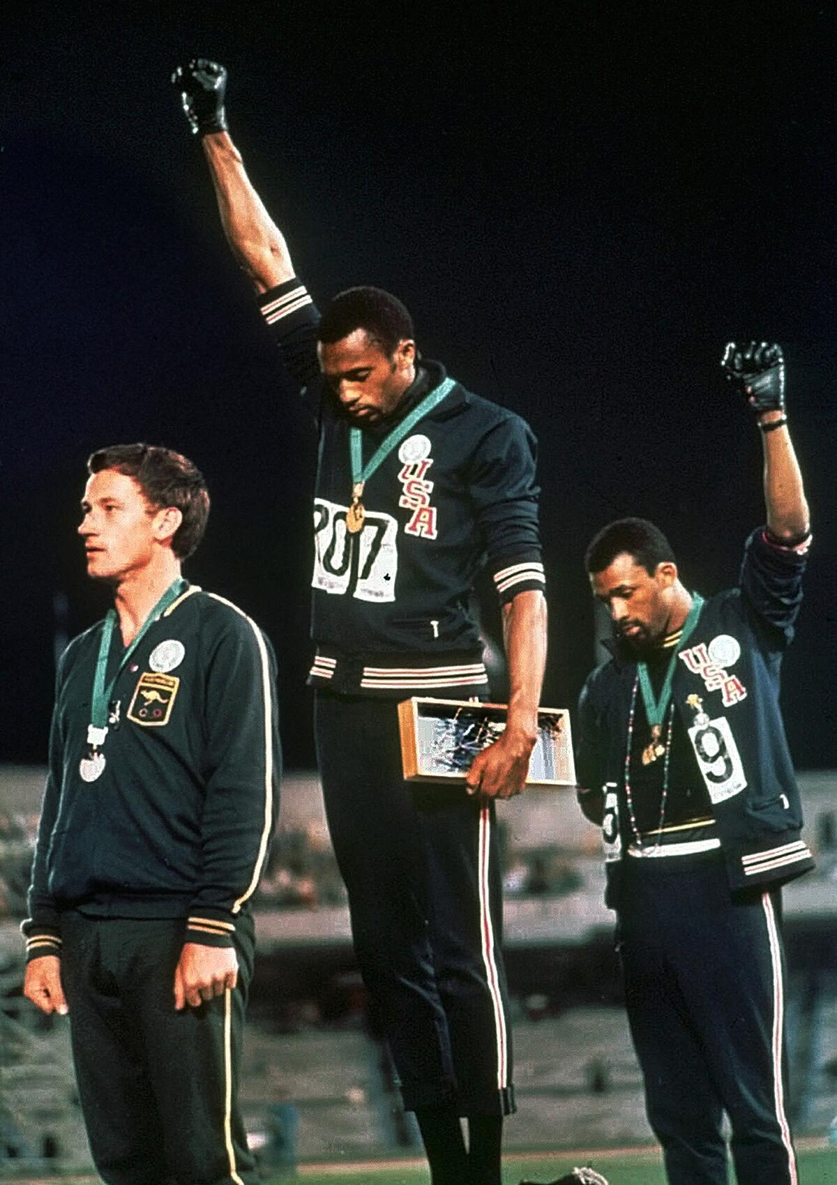 Three men standing on a podium, with two holding up their fists in the air.