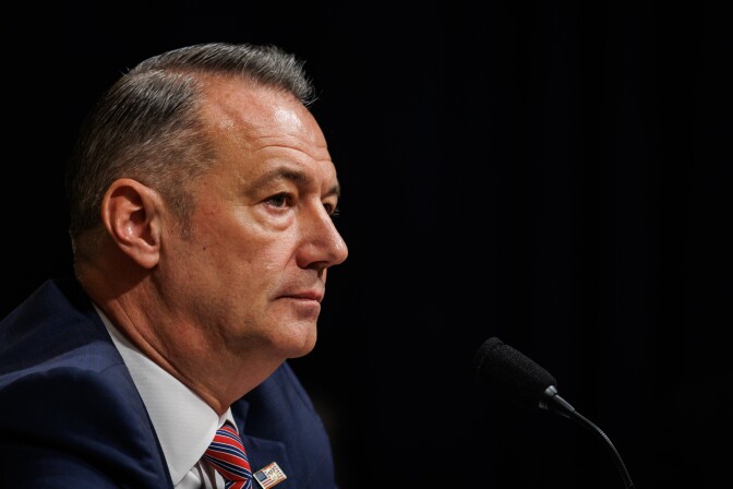 A man looks out of the frame and sits behind a microphone. 