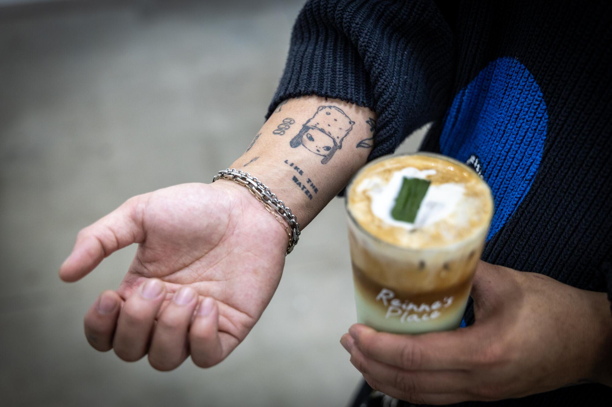 Reinne's Place owner Le holds one of his specialty drinks and shows his tattoos.