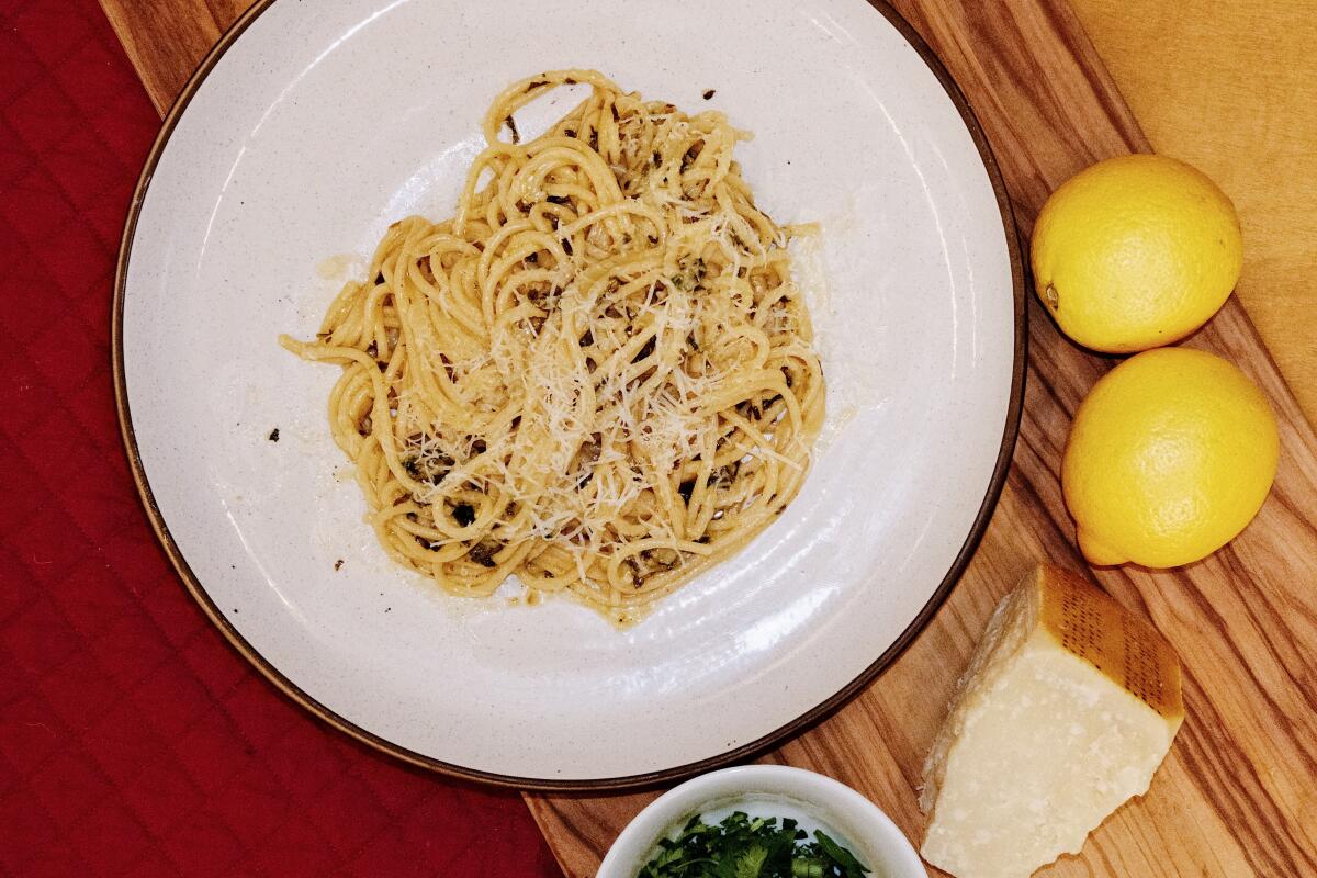 A plate of spaghetti al limone with lemons and cheese on wood and red fabric in the L.A. Times Test Kitchen.