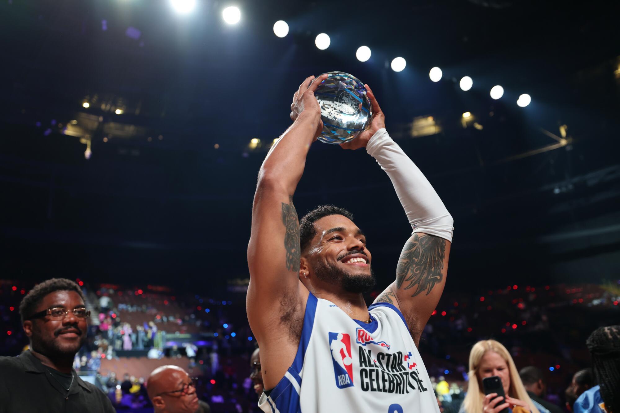 Actor Rome Flynn holds up a trophy and smiles after winning NBA all-star celebrity game MVP honors at the Kia Forum.