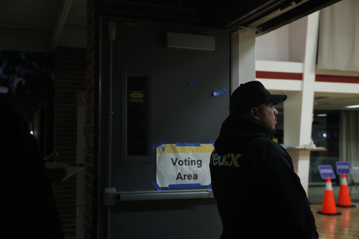 A man waits in line near a sign that reads "Voting Area."